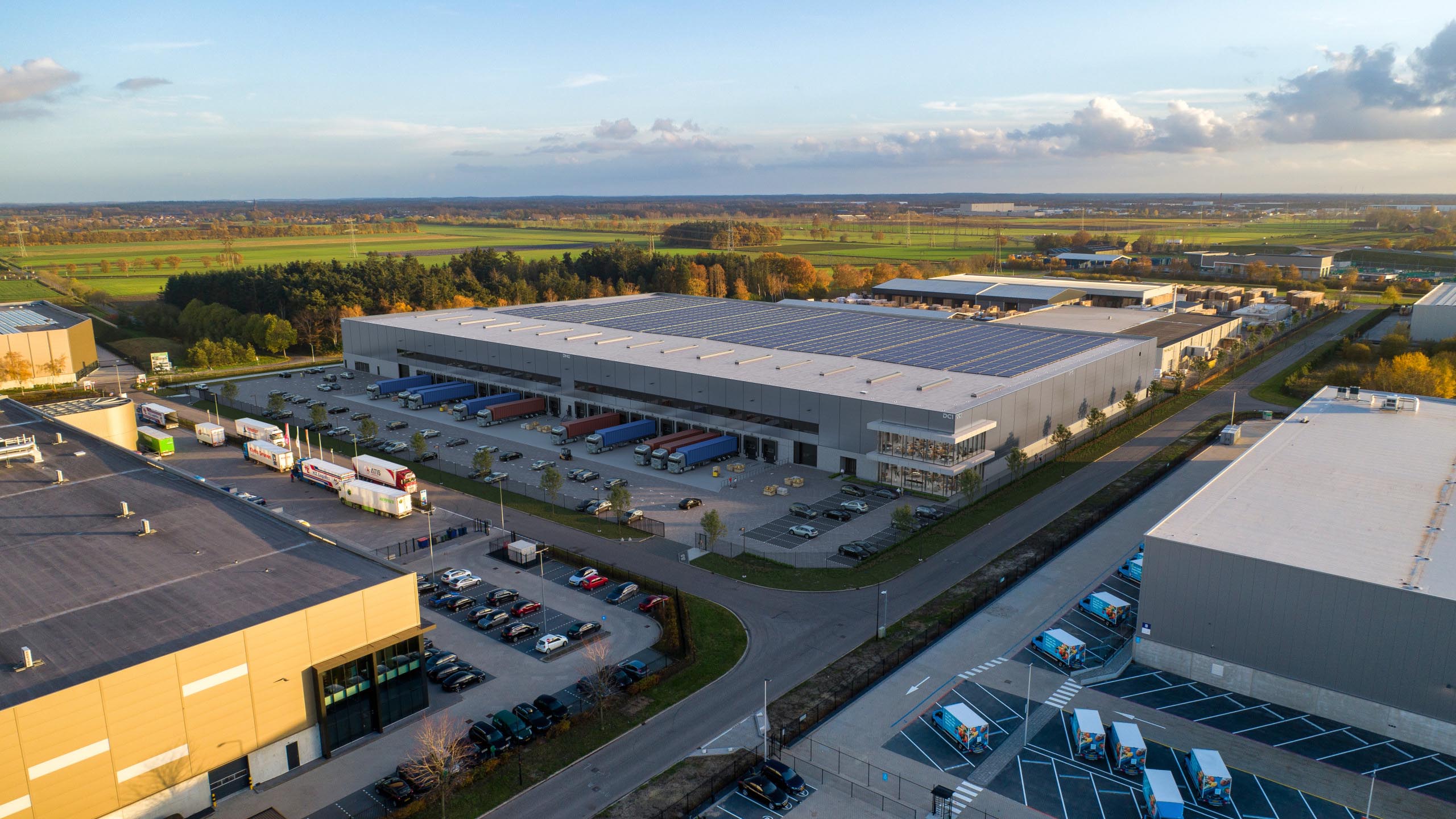 Oblique aerial view of DHG Smartlog Roosendaal with rooftop solar panels and loading bays in Oud-Gastel