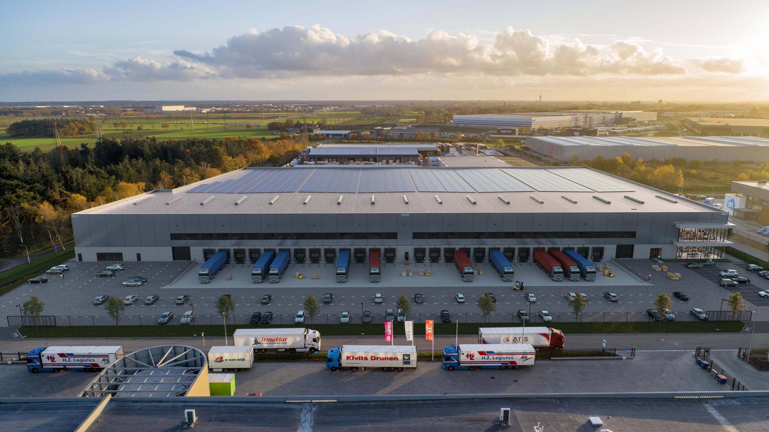 Elevated frontal view of DHG Smartlog Roosendaal showing loading docks, trucks, and rooftop photovoltaic panels