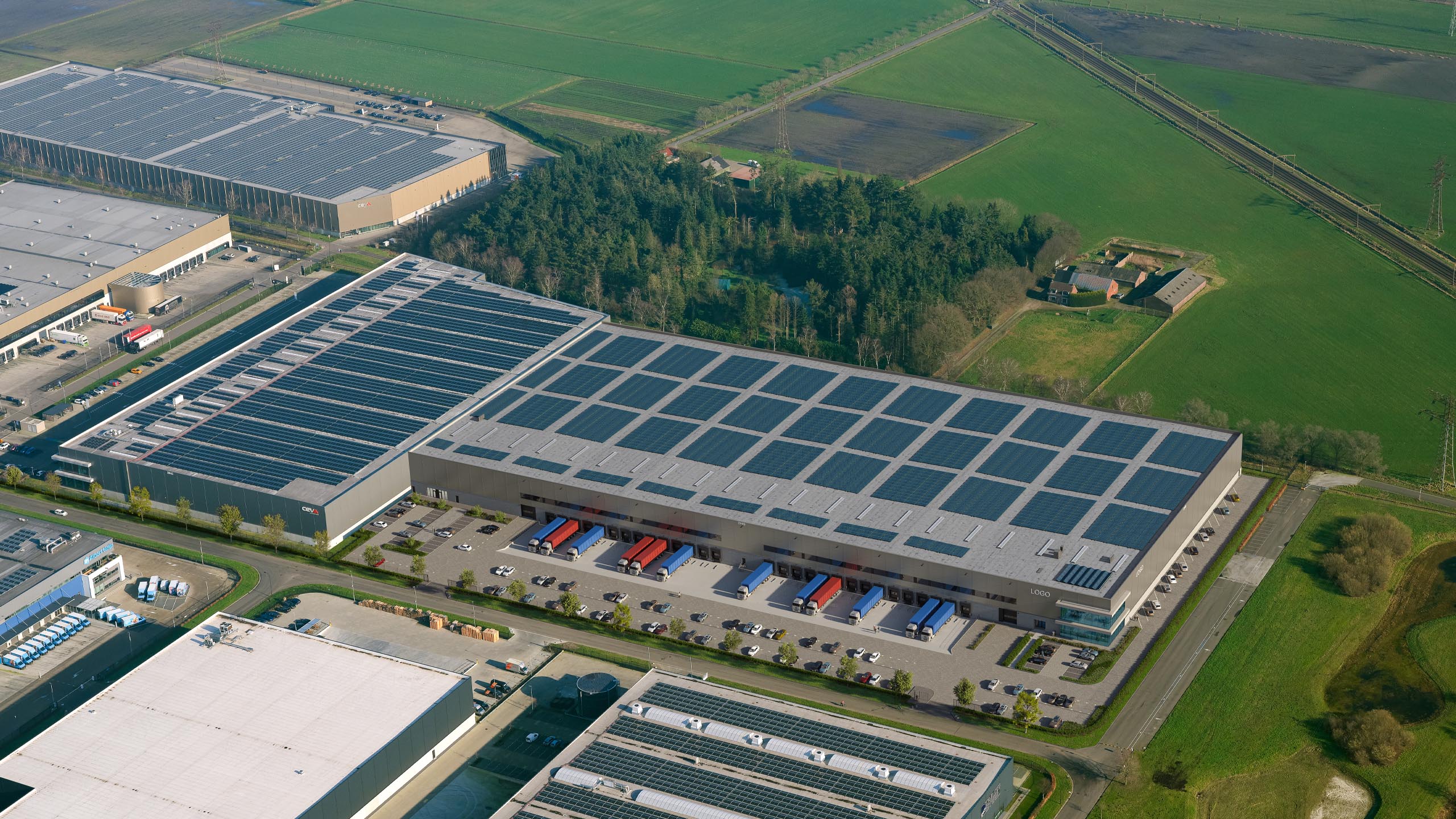High aerial view of DHG Smartlog Roosendaal beside neighbouring warehouses, woodland, and agricultural fields